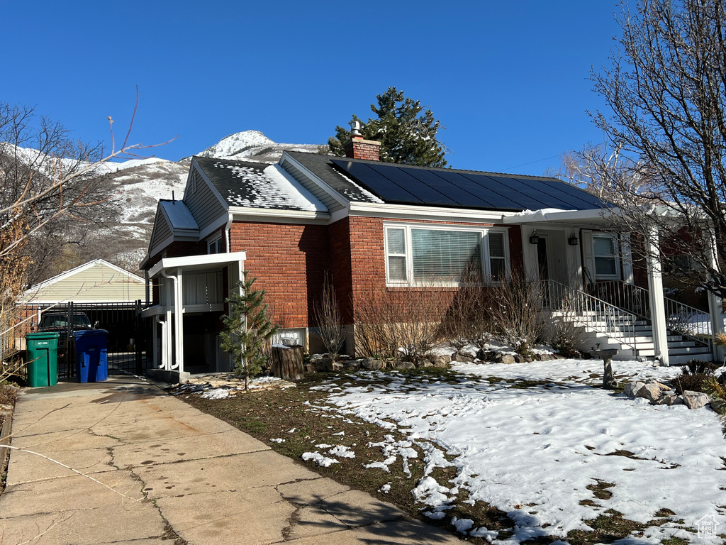 View of front of house with brick siding, solar panels, concrete driveway, a chimney, and a mountain view