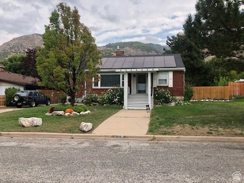 View of front of property with solar panels, a front yard, fence, and a mountain view