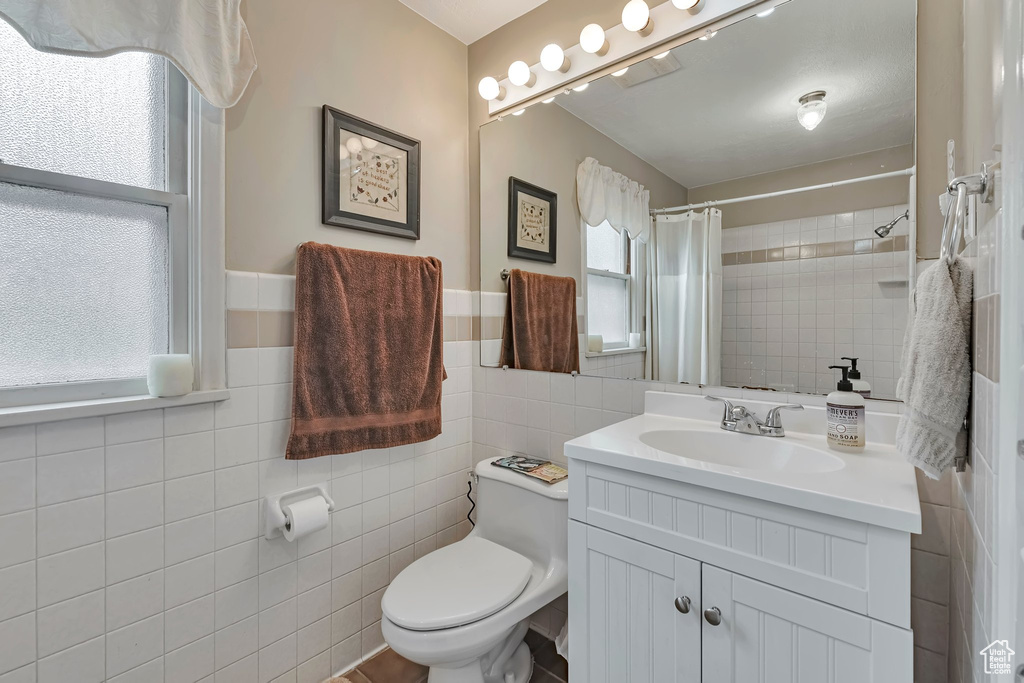 Bathroom featuring tile walls, plenty of natural light, vanity, toilet, and a shower with shower curtain