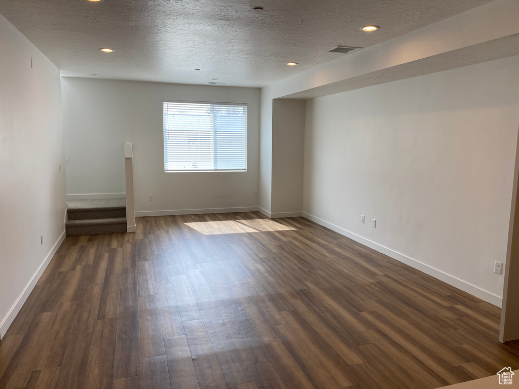 Empty room featuring baseboards, dark wood-style flooring, and a textured ceiling
