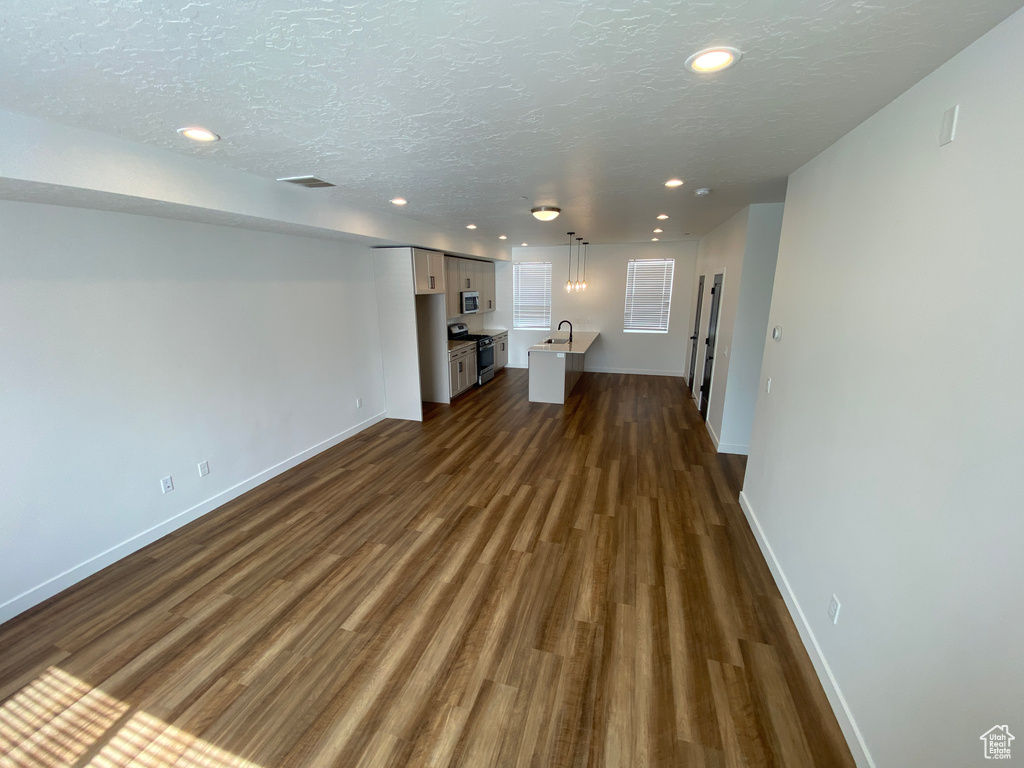 Unfurnished living room with dark wood-type flooring, baseboards, recessed lighting, a textured ceiling, and a sink