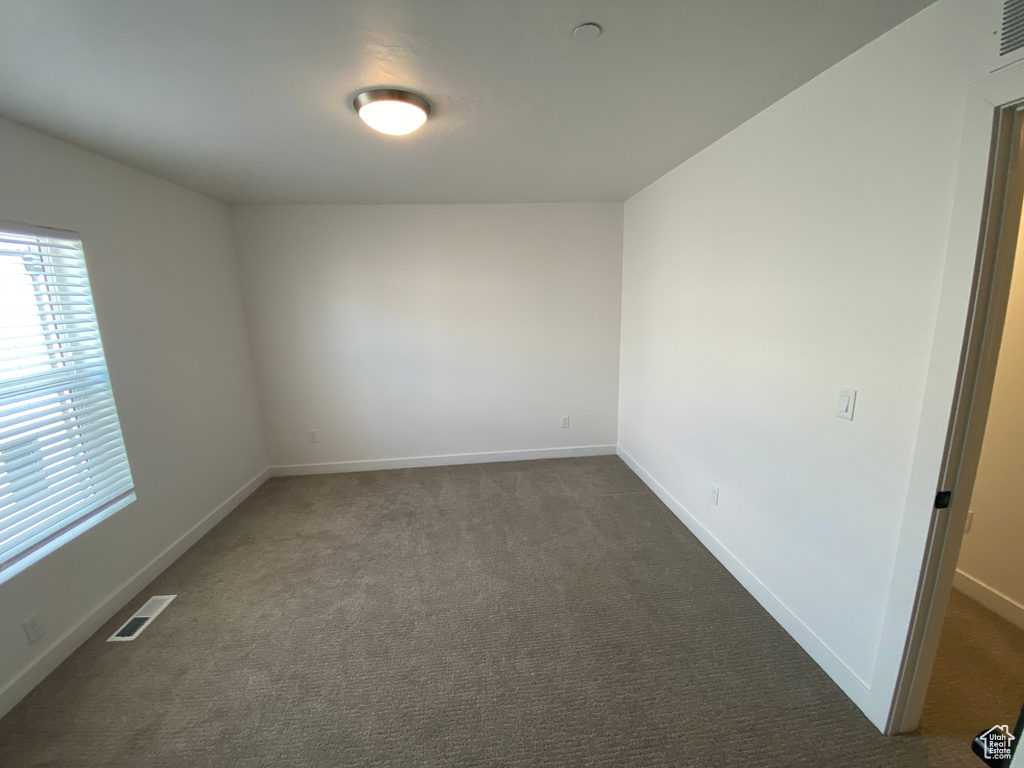Unfurnished room featuring visible vents, dark carpet, and baseboards