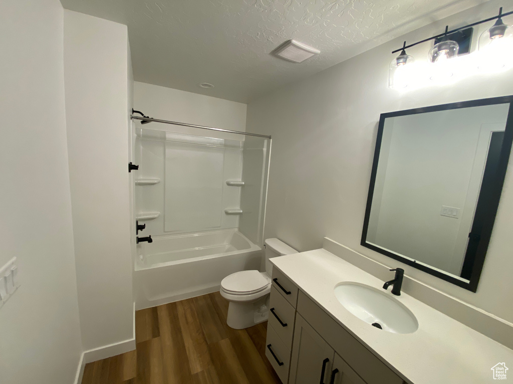 Full bath with vanity, a textured ceiling, wood finished floors, shower / washtub combination, and toilet
