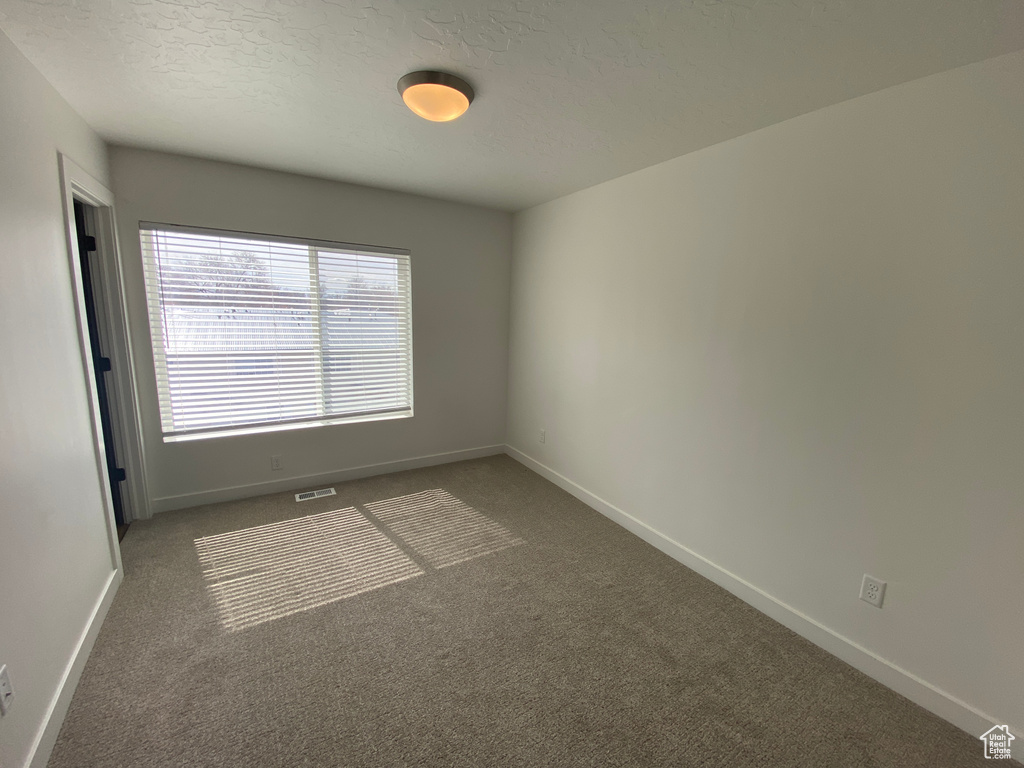 Carpeted spare room with visible vents, baseboards, and a textured ceiling