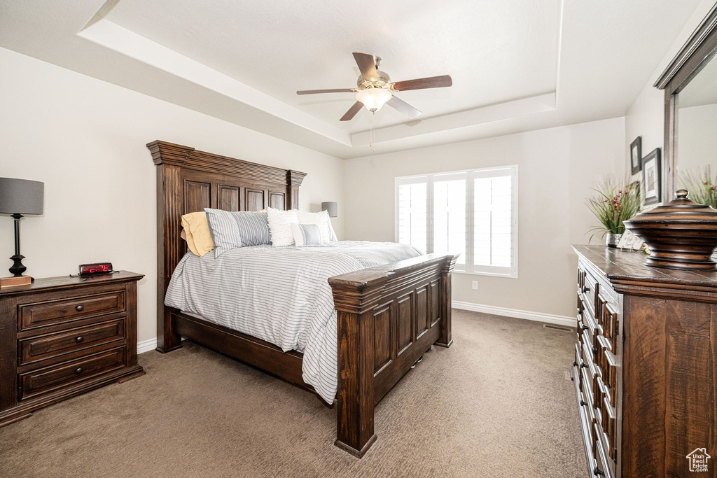 Carpeted bedroom featuring baseboards, a tray ceiling, and a ceiling fan