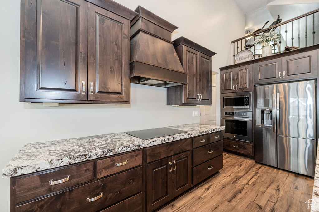 Kitchen with light wood finished floors, dark brown cabinetry, custom range hood, a towering ceiling, and stainless steel appliances