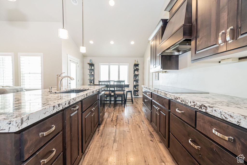 Kitchen with light stone counters, custom exhaust hood, a sink, vaulted ceiling, and black electric stovetop