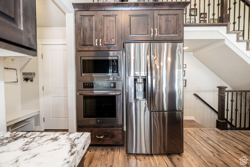 Kitchen with stainless steel appliances, light stone countertops, light wood-style floors, and dark brown cabinets