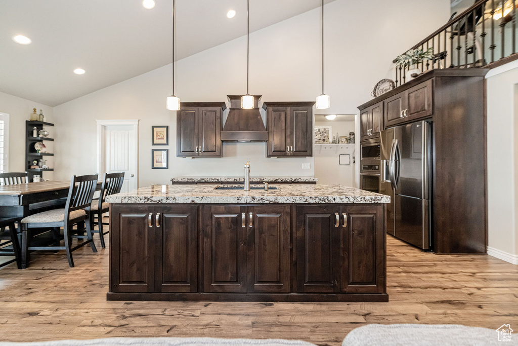 Kitchen with light wood finished floors, dark brown cabinetry, appliances with stainless steel finishes, and custom range hood