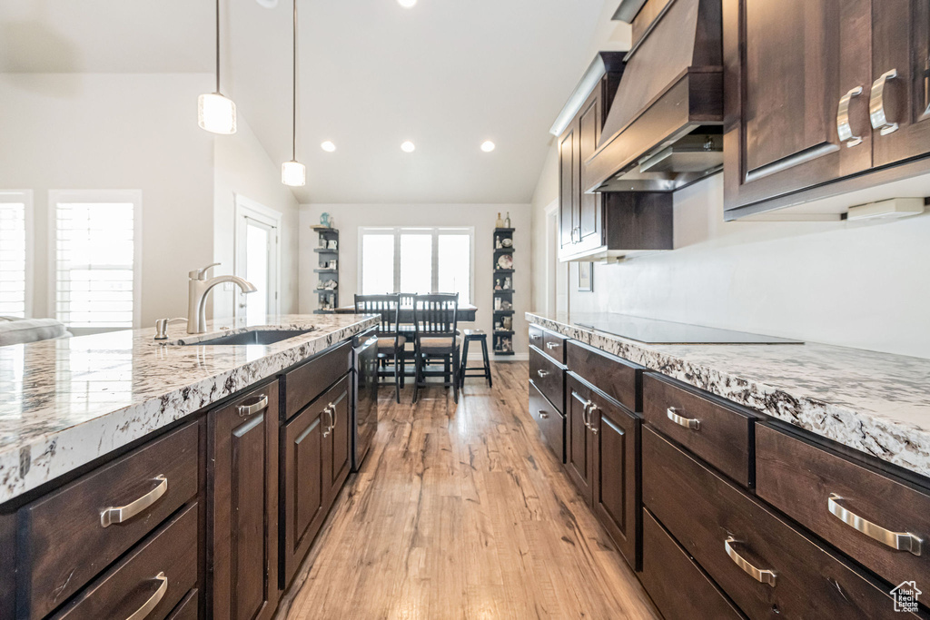 Kitchen with premium range hood, light stone counters, lofted ceiling, and a sink