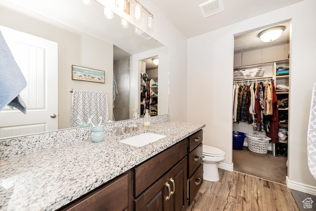 Bathroom featuring vanity, wood finished floors, visible vents, a spacious closet, and toilet