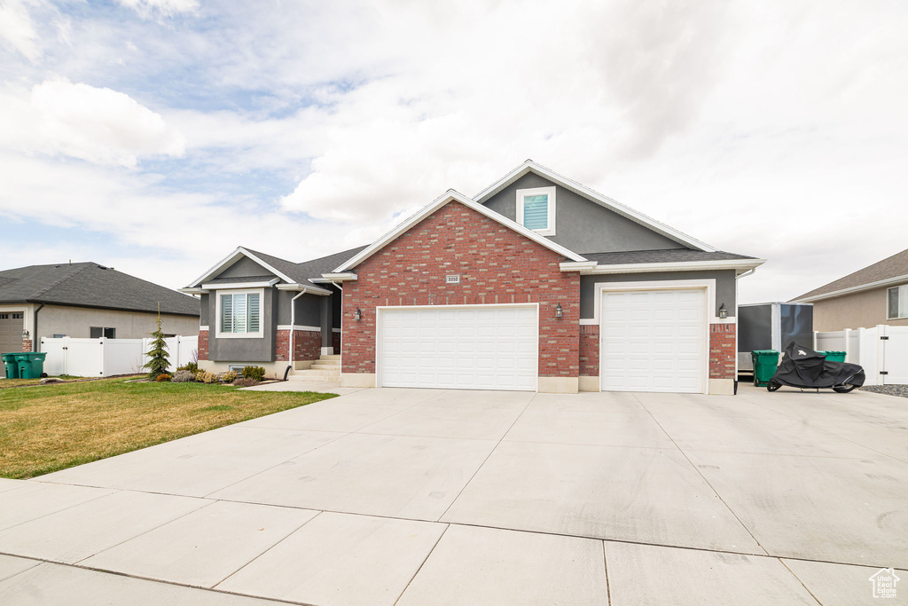 View of front of house featuring a front yard, fence, concrete driveway, a garage, and brick siding