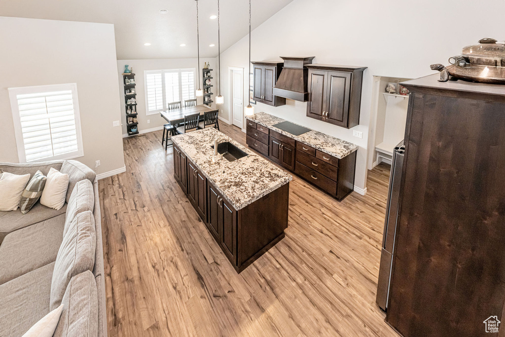Kitchen with light wood-type flooring, an island with sink, refrigerator, open floor plan, and dark brown cabinets
