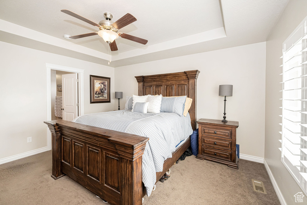 Bedroom with visible vents, ceiling fan, baseboards, light carpet, and a raised ceiling