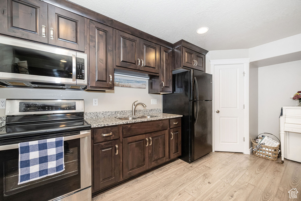 Kitchen with dark brown cabinets, light stone counters, light wood-style flooring, appliances with stainless steel finishes, and a sink
