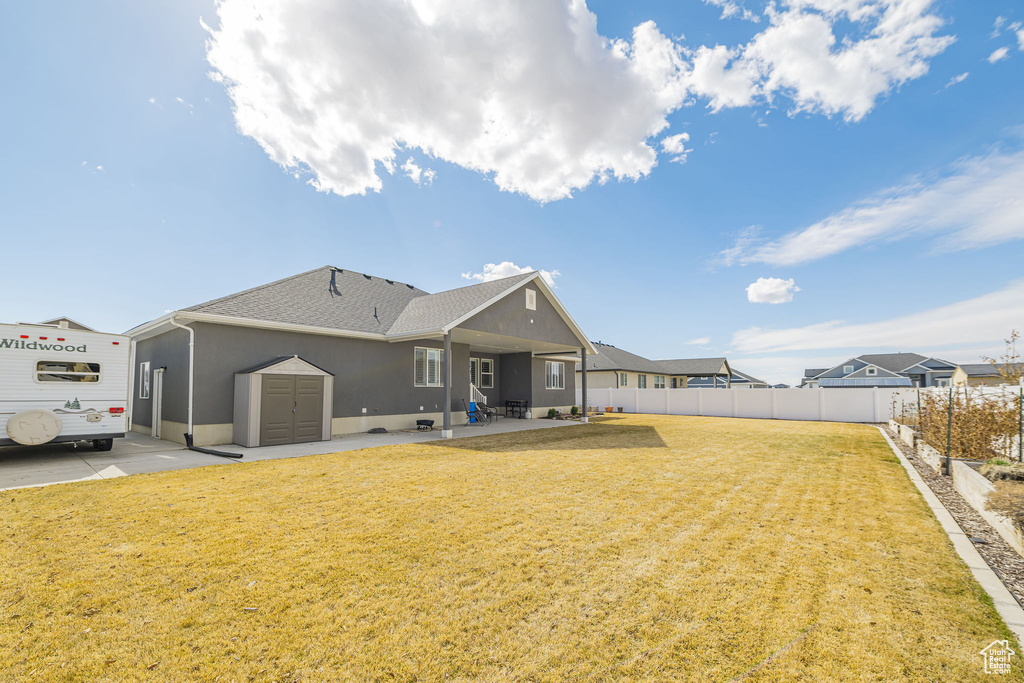 Back of property featuring fence, a patio area, a lawn, and a shingled roof