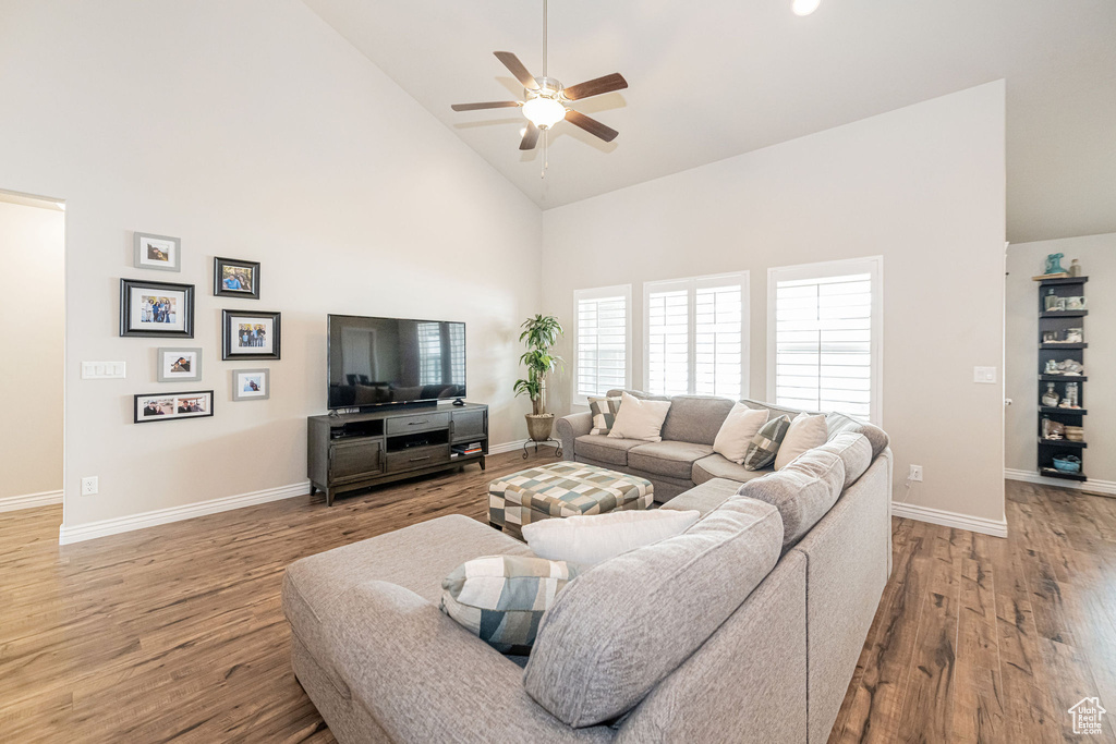 Living room with ceiling fan, wood finished floors, baseboards, and high vaulted ceiling
