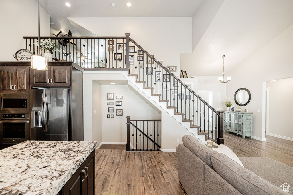 Kitchen with wood finished floors, high vaulted ceiling, appliances with stainless steel finishes, and dark brown cabinetry