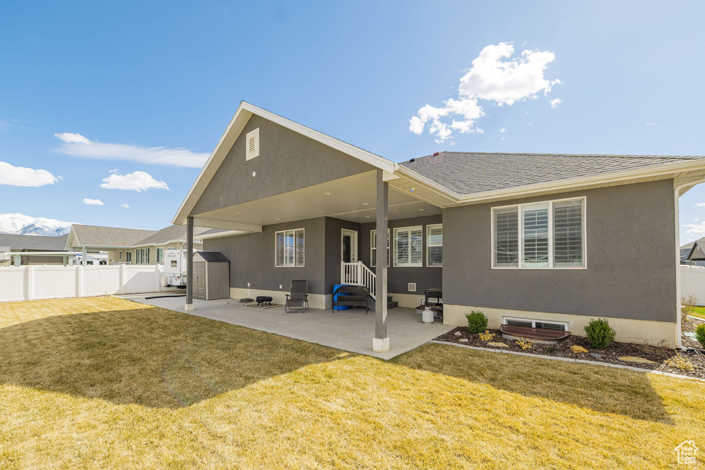 Rear view of house featuring a yard, a storage unit, a patio, and fence