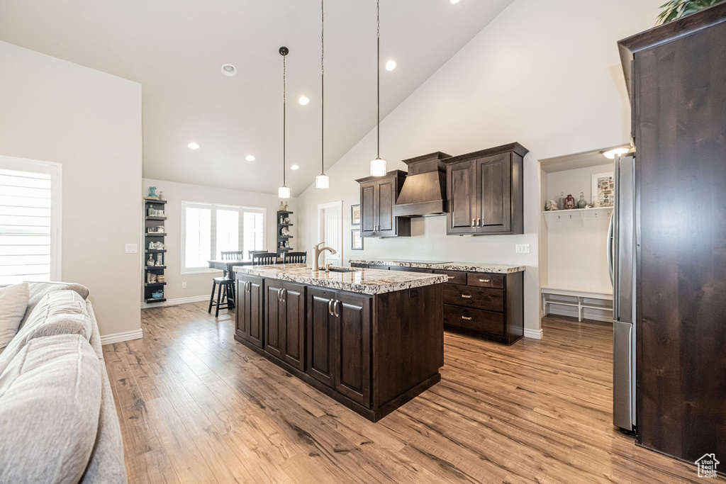 Kitchen with a sink, custom exhaust hood, dark brown cabinets, and open floor plan