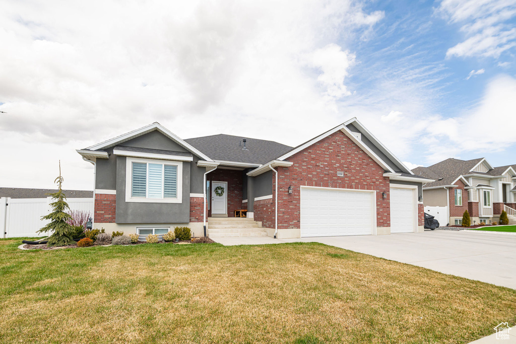 View of front of property with driveway, a front lawn, fence, an attached garage, and brick siding