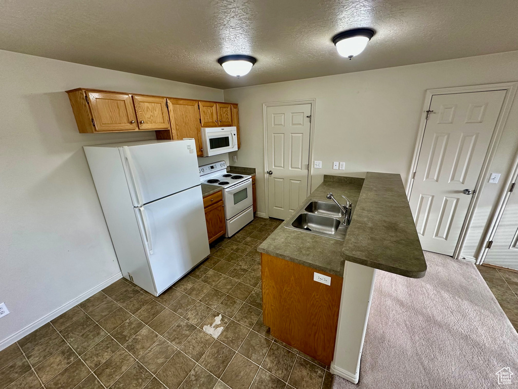 Kitchen featuring a sink, baseboards, white appliances, and a peninsula