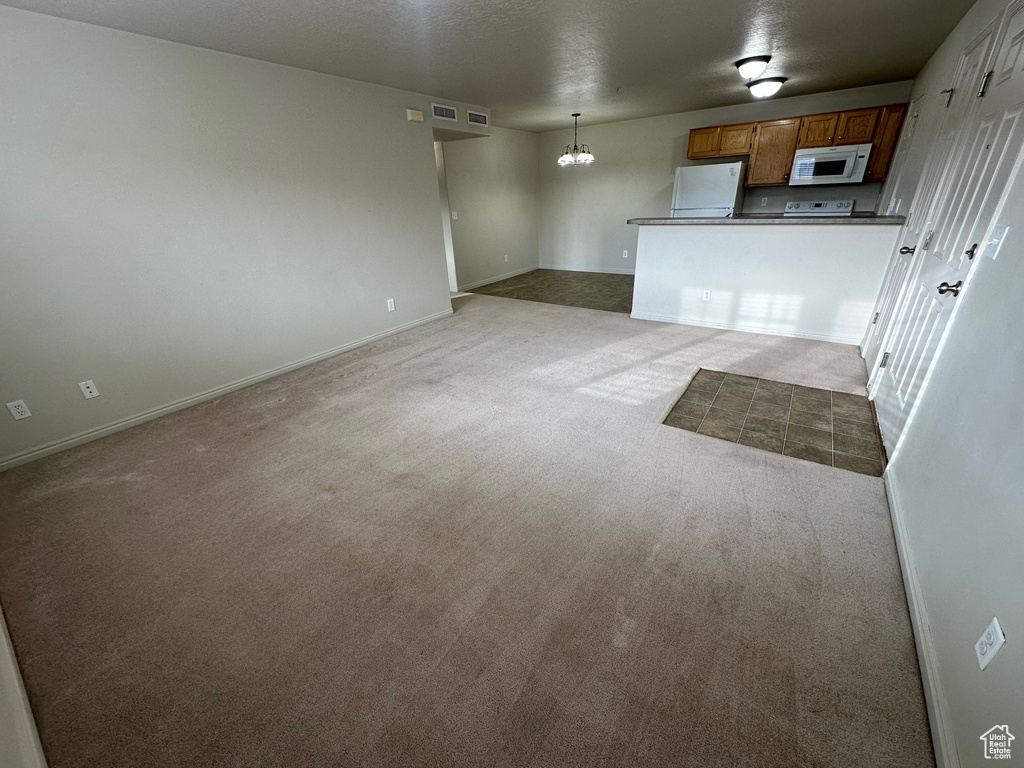 Unfurnished living room with an inviting chandelier, carpet flooring, visible vents, and baseboards