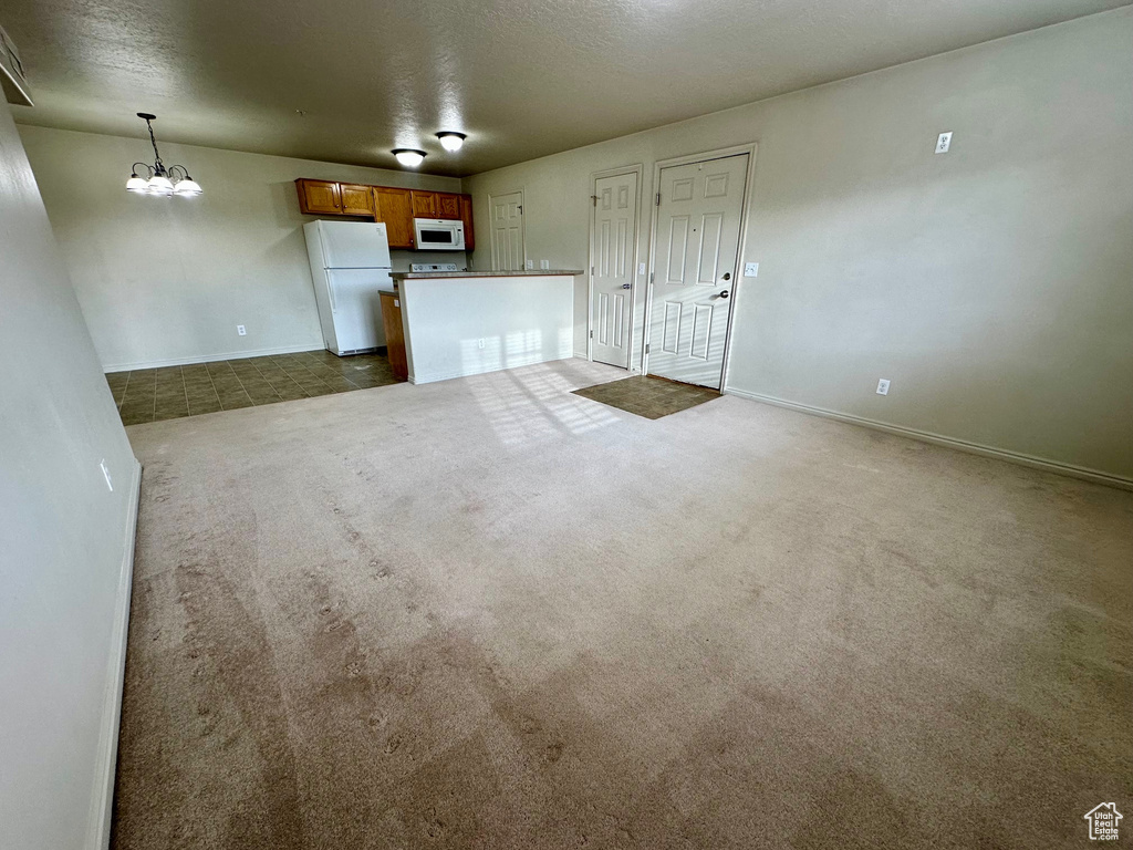 Unfurnished living room with a notable chandelier, dark carpet, a textured ceiling, and baseboards