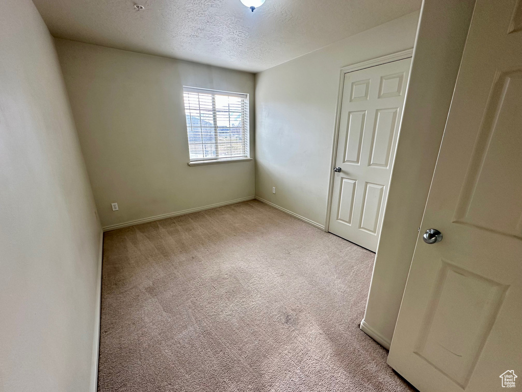 Unfurnished bedroom with light carpet, a textured ceiling, and baseboards