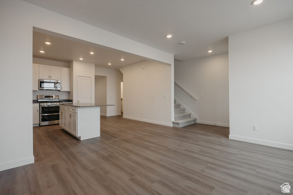 Kitchen featuring stainless steel appliances, wood finished floors, open floor plan, and white cabinetry