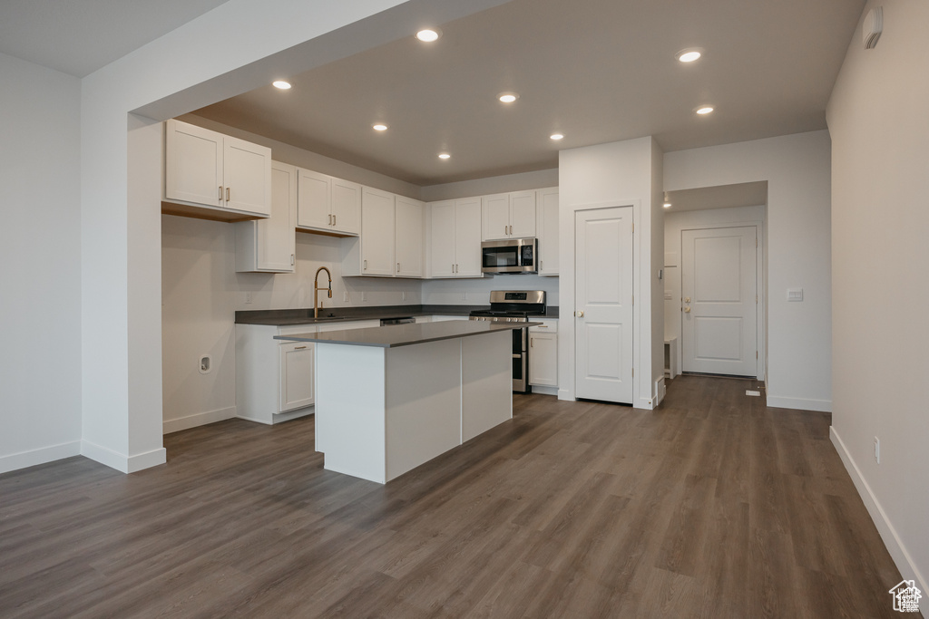 Kitchen featuring a kitchen island, recessed lighting, stainless steel appliances, dark wood-type flooring, and white cabinets