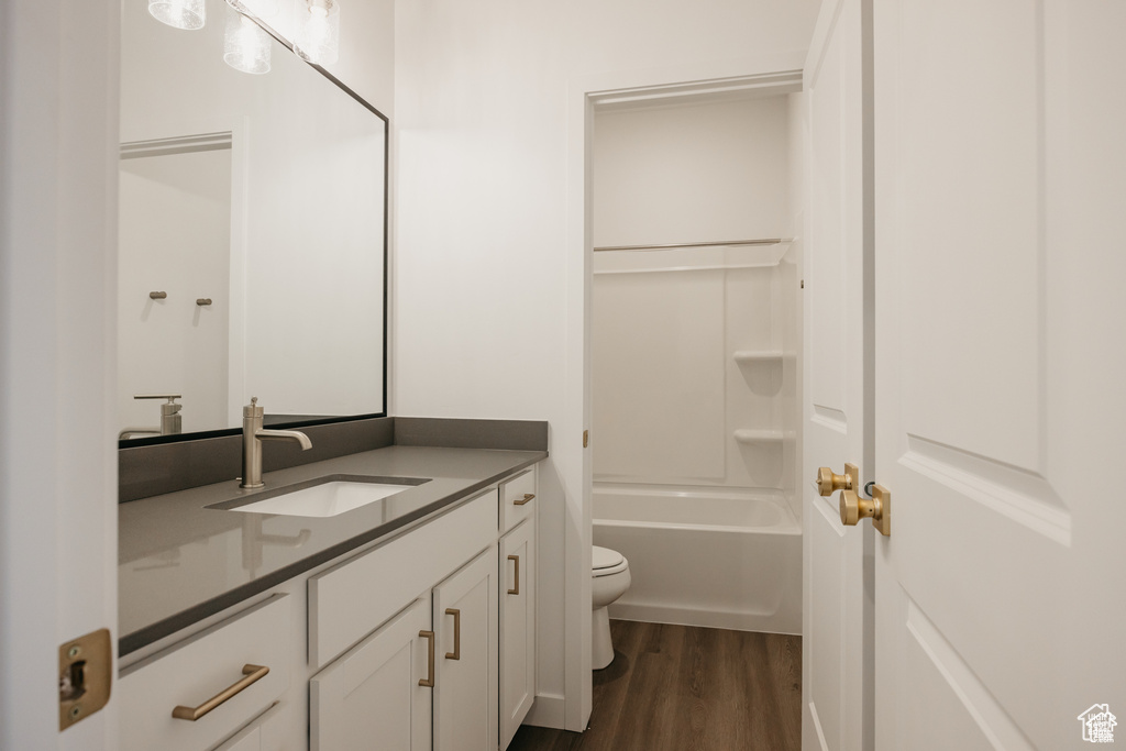 Bathroom featuring toilet,  shower combination, wood finished floors, and vanity