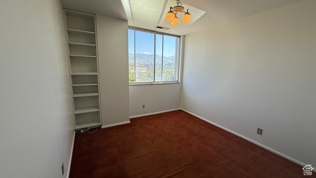 Spare room with dark carpet, a chandelier, and baseboards
