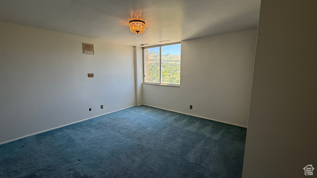 Unfurnished room featuring dark colored carpet, baseboards, and a chandelier