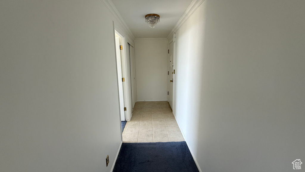 Corridor featuring light tile patterned flooring, baseboards, crown molding, and light colored carpet