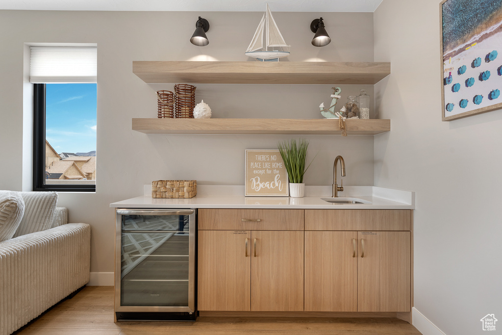 Bar featuring baseboards, wet bar, light wood-style flooring, a sink, and wine cooler