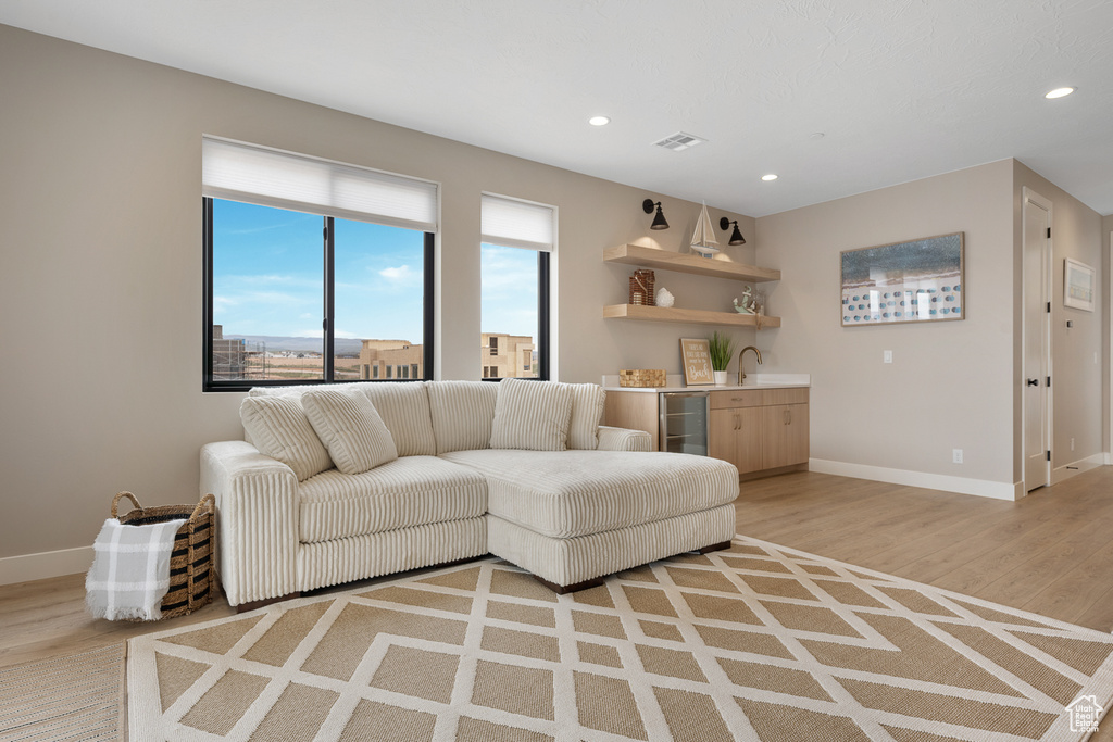 Living room with light wood-type flooring, visible vents, beverage cooler, indoor wet bar, and baseboards