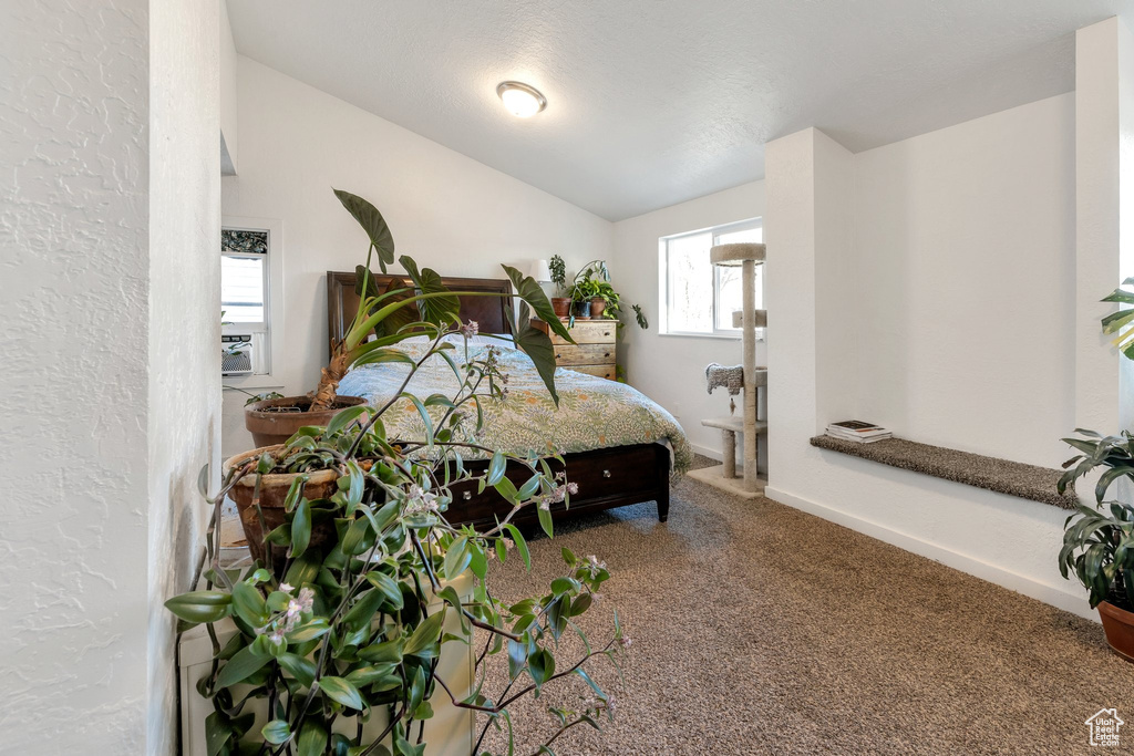 Bedroom with cooling unit, carpet, baseboards, vaulted ceiling, and a textured wall