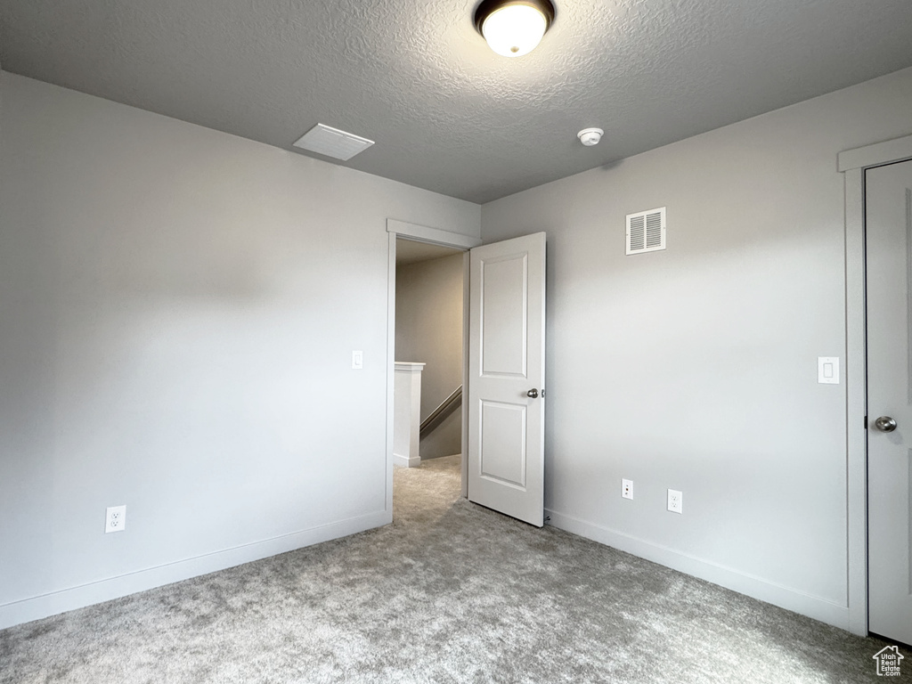Spare room featuring visible vents, carpet flooring, a textured ceiling, and baseboards