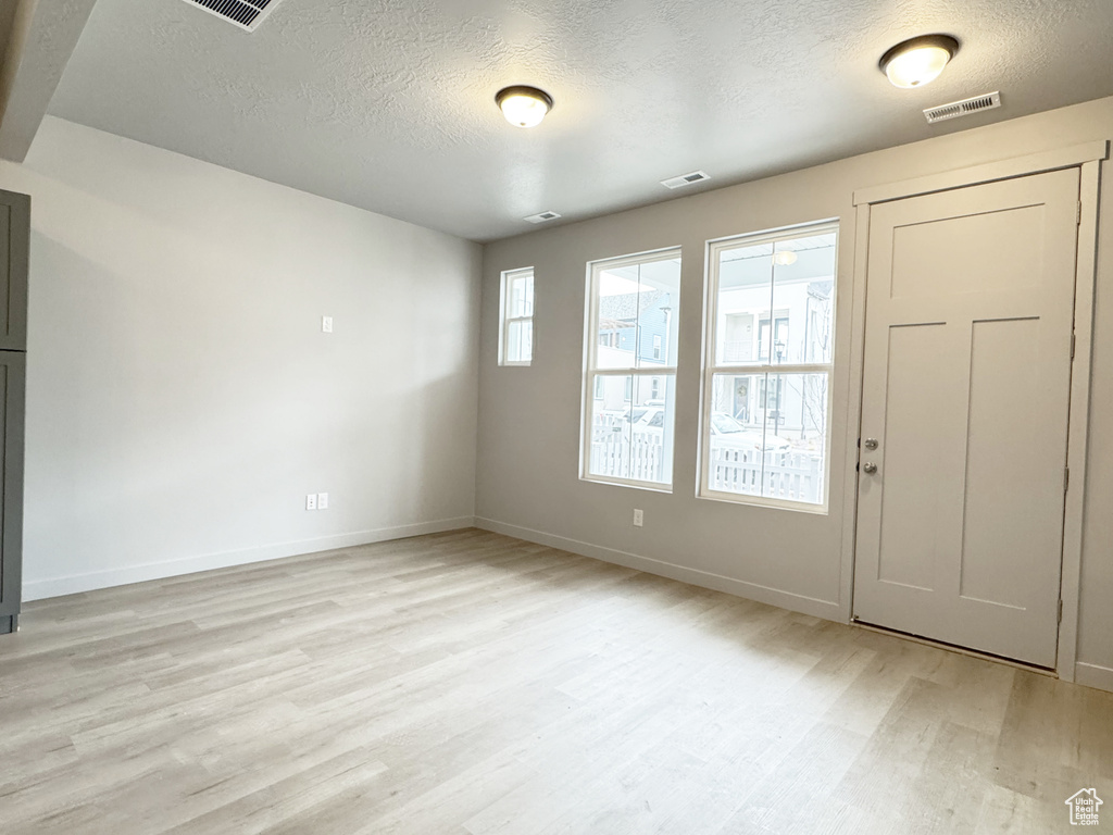 Unfurnished room with a textured ceiling, visible vents, light wood-type flooring, and baseboards