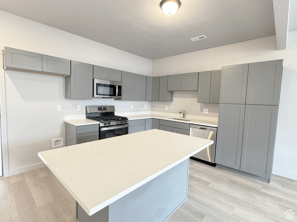 Kitchen featuring visible vents, gray cabinets, a sink, appliances with stainless steel finishes, and light wood-type flooring