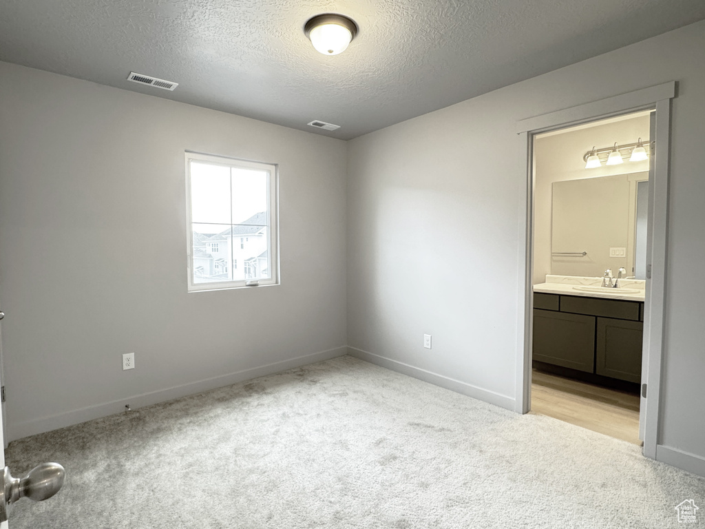 Unfurnished bedroom with a sink, visible vents, light colored carpet, and a textured ceiling