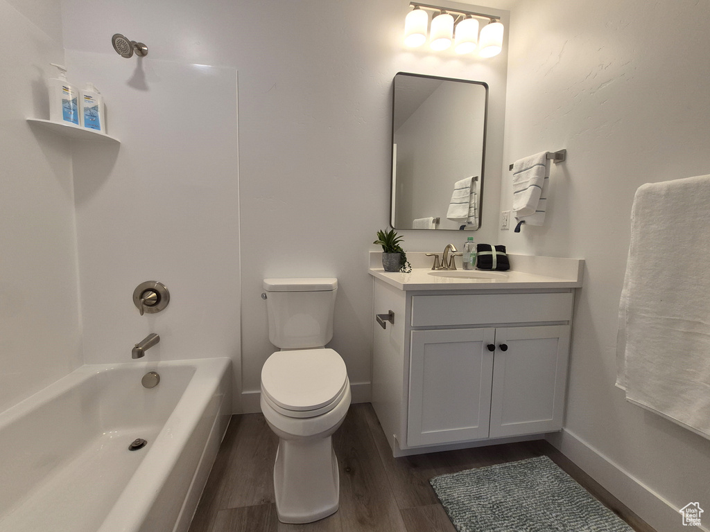 Bathroom with baseboards, toilet, shower / bathing tub combination, wood finished floors, and vanity