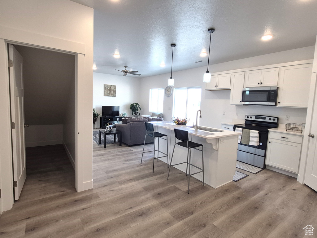 Kitchen featuring light wood finished floors, a breakfast bar, appliances with stainless steel finishes, white cabinetry, and a sink