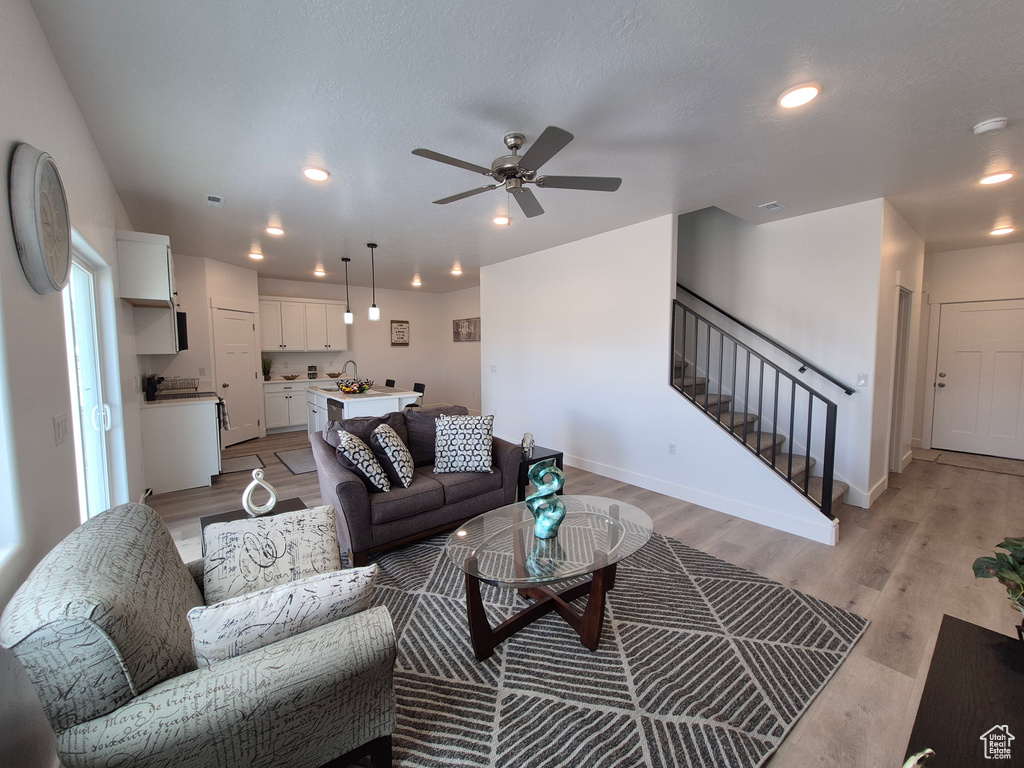 Living area featuring light wood-type flooring, baseboards, ceiling fan, and stairs