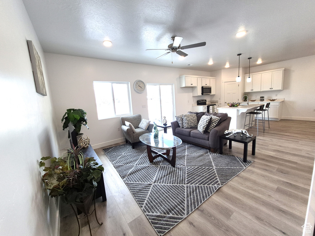 Living room with light wood-type flooring, baseboards, a textured ceiling, and a ceiling fan