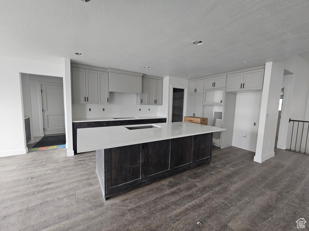 Kitchen with dark wood-style floors, baseboards, cooktop, and a large island with sink