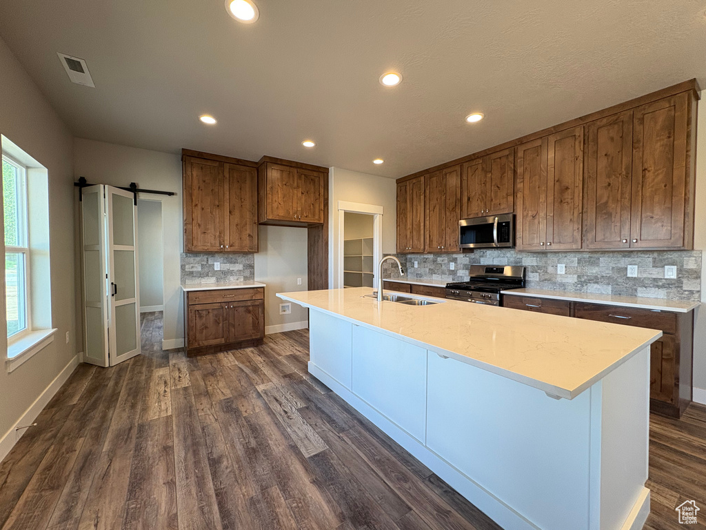 Kitchen with appliances with stainless steel finishes, a sink, a barn door, brown cabinets, and decorative backsplash