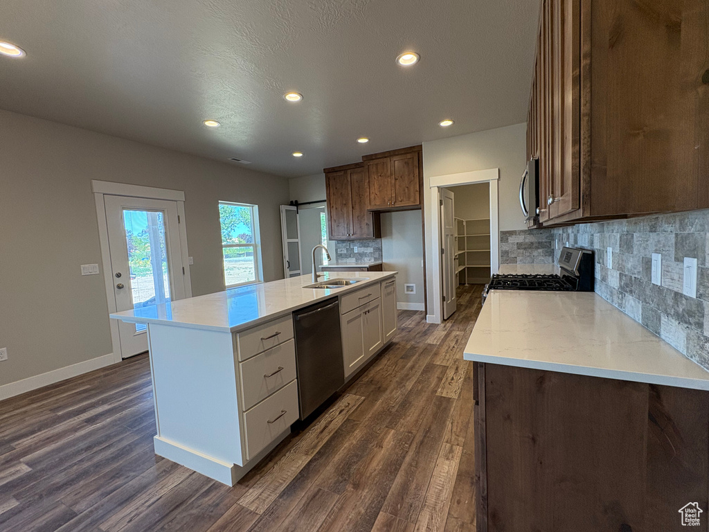 Kitchen featuring appliances with stainless steel finishes, a sink, dark wood finished floors, tasteful backsplash, and baseboards
