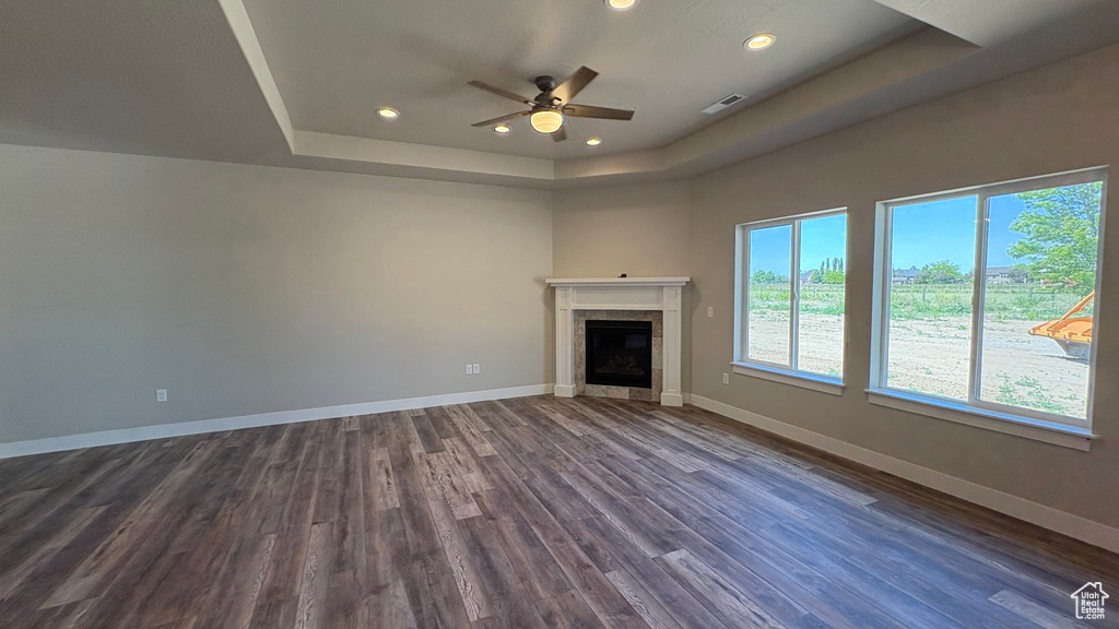 Unfurnished living room featuring a raised ceiling, a ceiling fan, dark wood-style flooring, recessed lighting, and baseboards